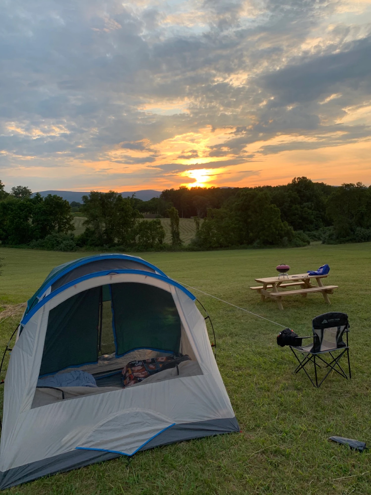 A tent in the foreground with a picnic table and a dramatic Virginia sunset breaking through the clouds