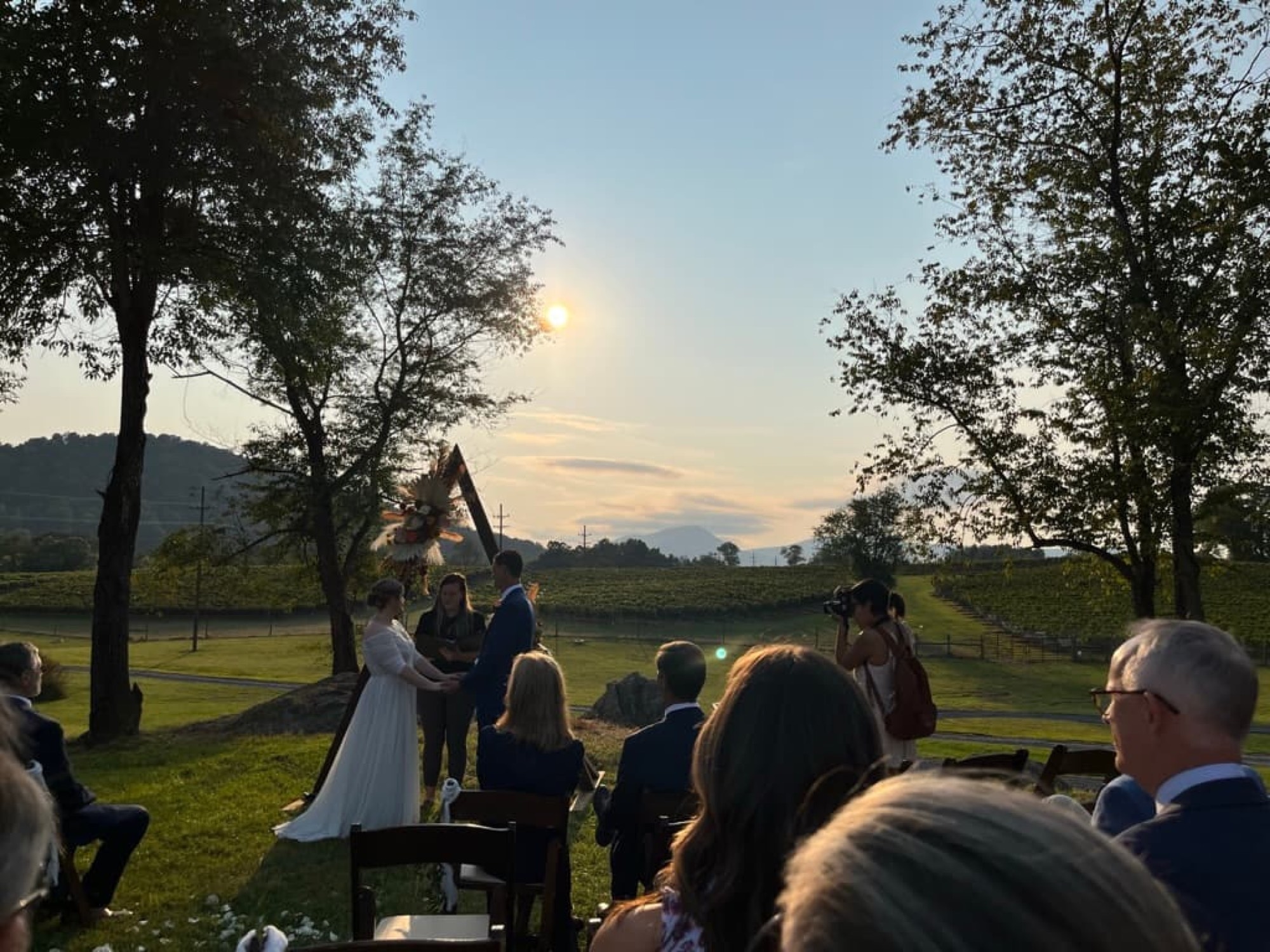 An evening gathering on the lawn at sunset with guests seated, vineyard rows and mountains in the background